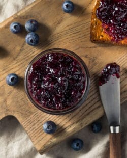Blueberry jam in a jar as seen from overhead with spreader and toast.