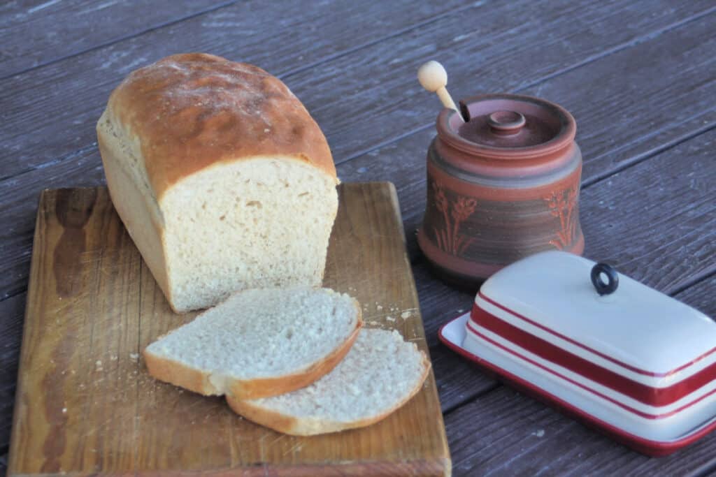 A loaf and slices of peanut butter bread on a cutting board sitting next to a butter dish and pot of honey.