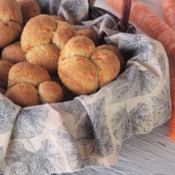 Carrot cloverleaf rolls stacked inside a napkin lined basket.