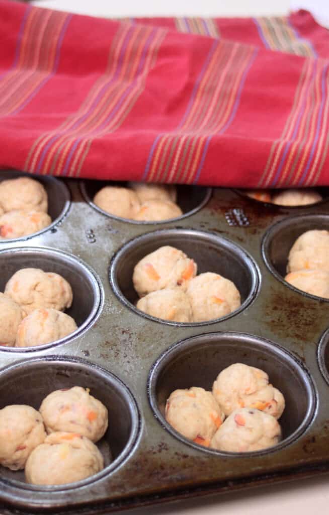 Balls of carrot cloverleaf roll dough inside muffin tin cups ready to rise.