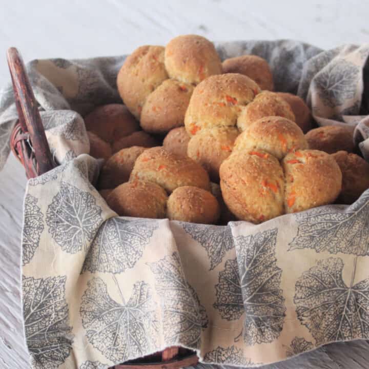 Carrot cloverleaf rolls stacked inside a napkin lined basket.