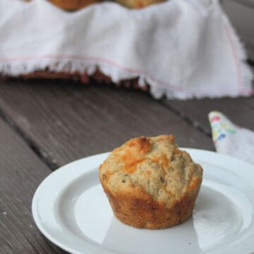 A cheddar rye muffin on a white with napkin sitting in front of a basket of muffins.