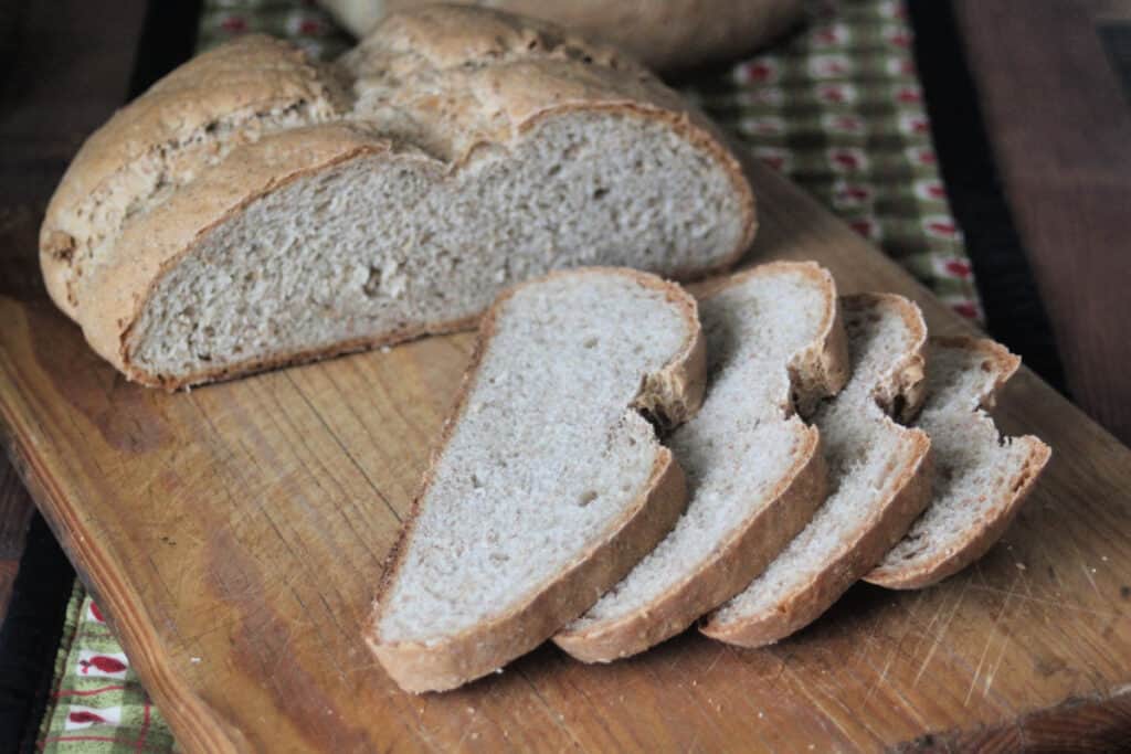 4 slices of rye bread sitting in front of entire loaf on a wood cutting board.