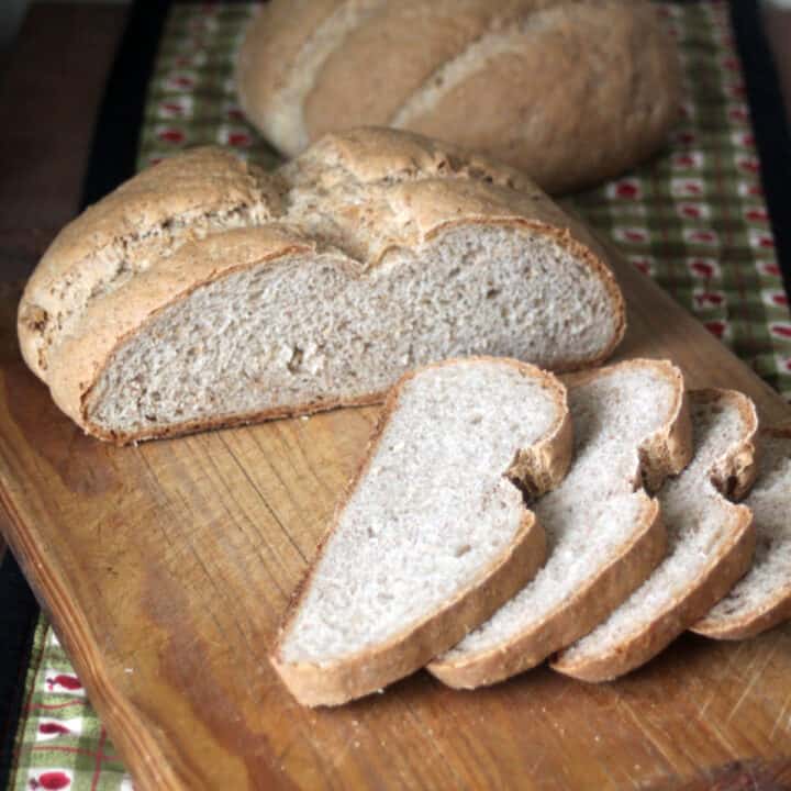 Slices of rye bread on a wooden board sitting front of remaining loaf.