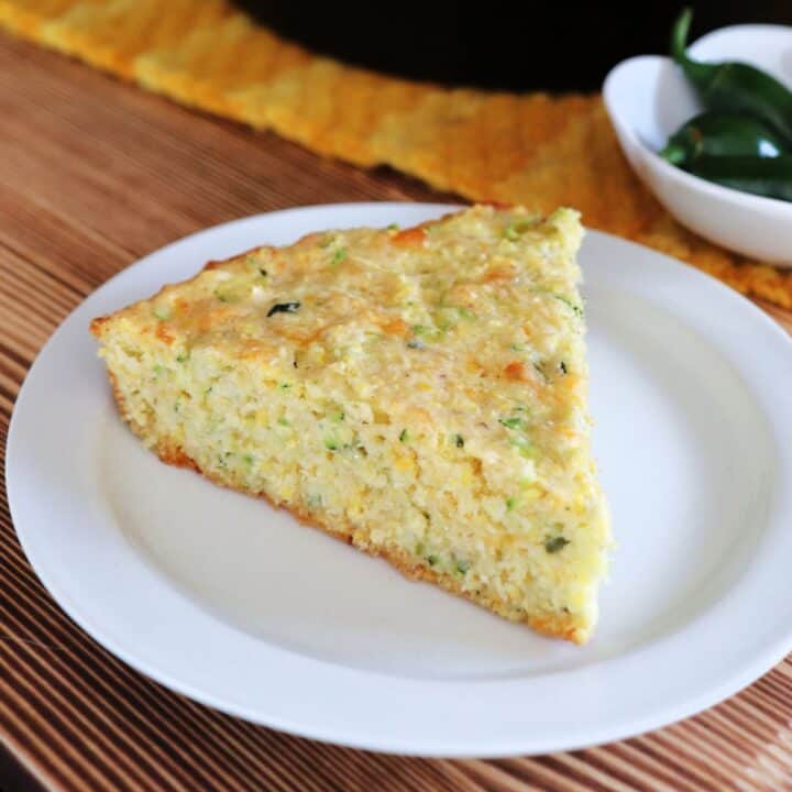 A triangular piece of zucchini cornbread sits on a white plate.