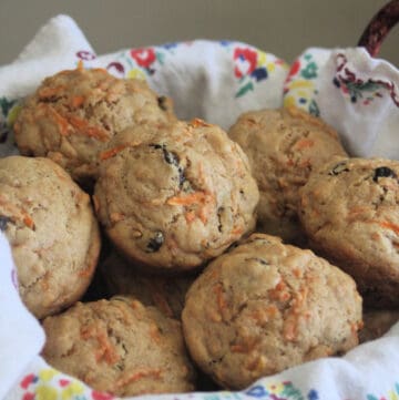 Carrot muffins stacked inside a floral napkin lined basket.