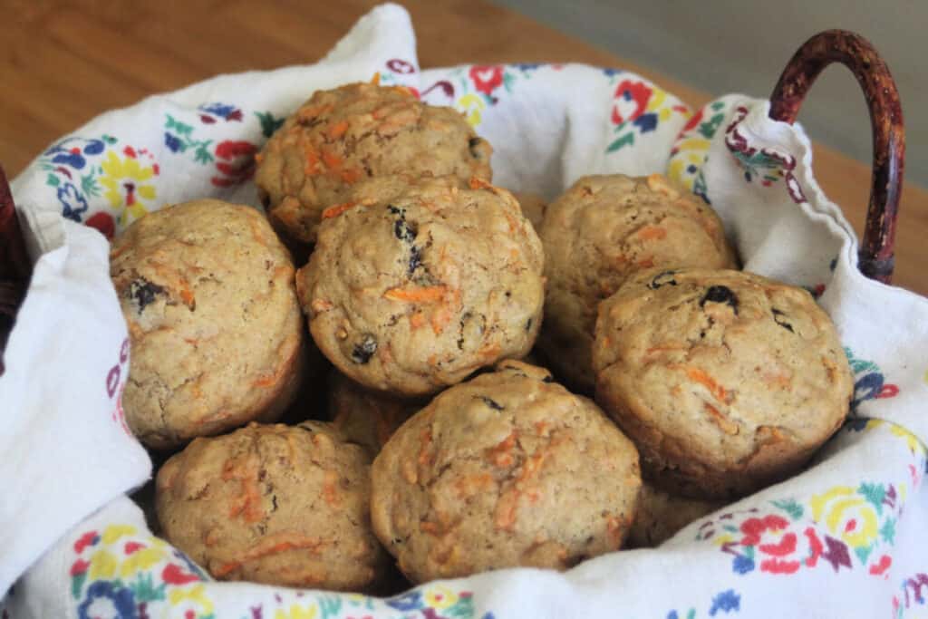 Carrot muffins stacked inside a floral napkin lined basket.