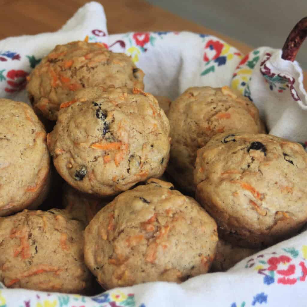 carrot raisin muffins stacked in a napkin lined basket.