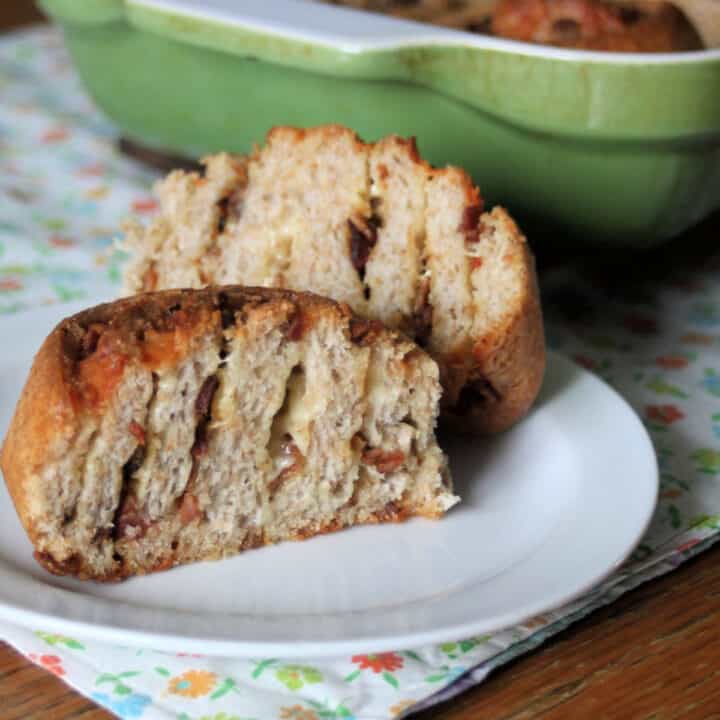 A cheddar bacon roll sliced in half sitting on a white plate.