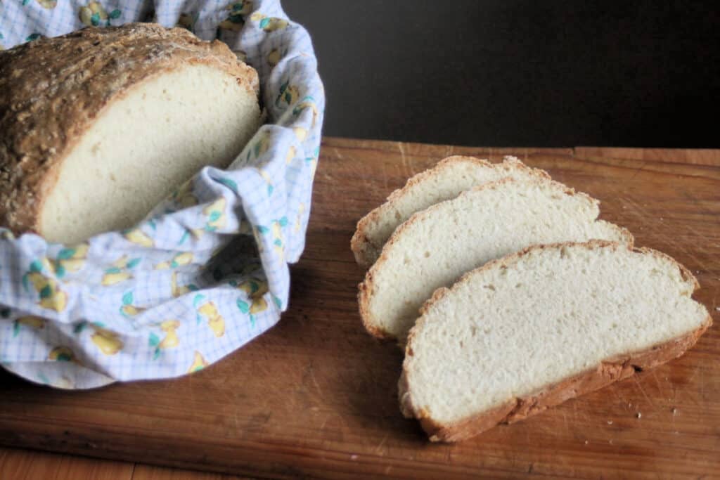 Slices of irish soda bread on a cutting board sitting next to a linen lined basket with the rest of the loaf sitting inside.