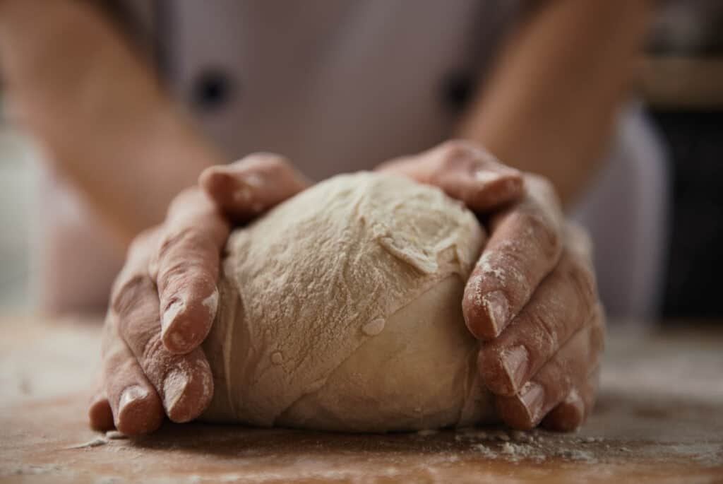 Male hands encasing a ball of bread dough on a wooden board.