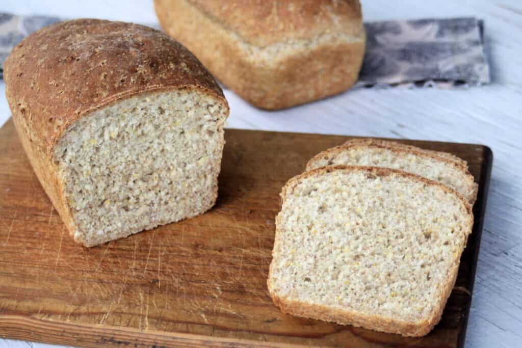 A loaf of mulitgrain bread and slices sitting on a wood cutting board.