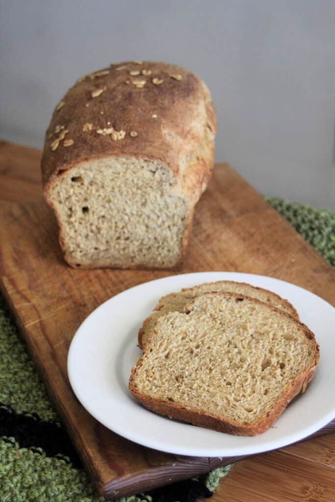 Slices of oatmeal bread on a white plate with loaf on a cutting board.