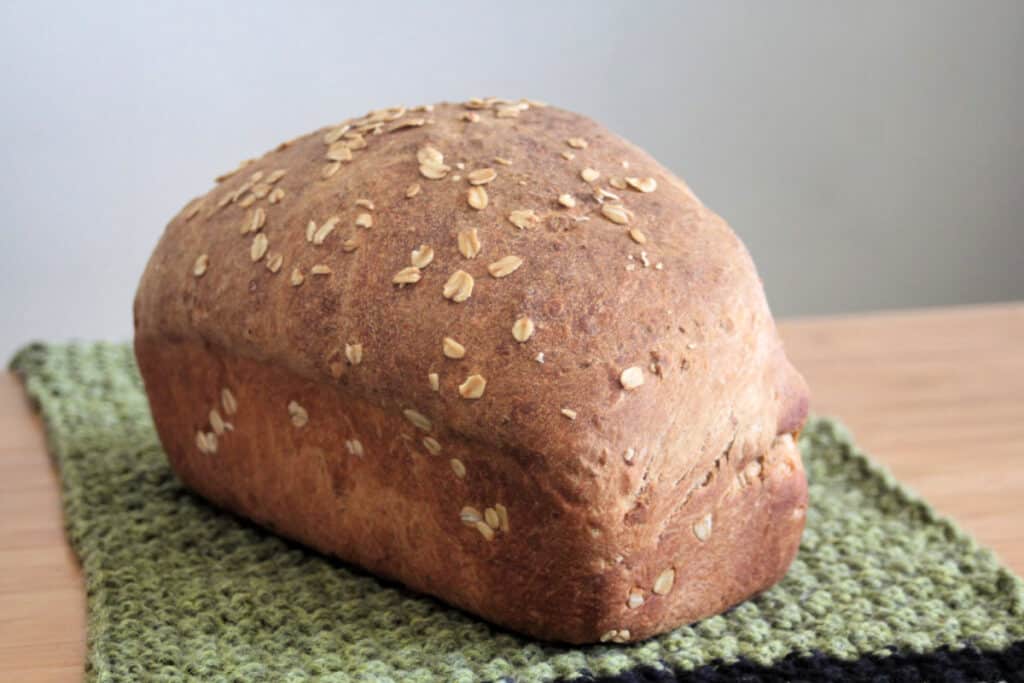 Loaf of oatmeal bread sitting on green knitted table runner.