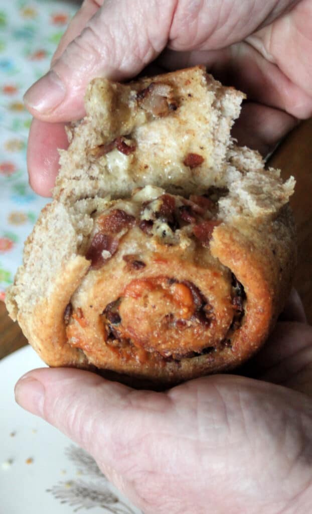 A man's hands pulling apart the layers of a cheddar bacon roll, exposing the bits of bacon inside.