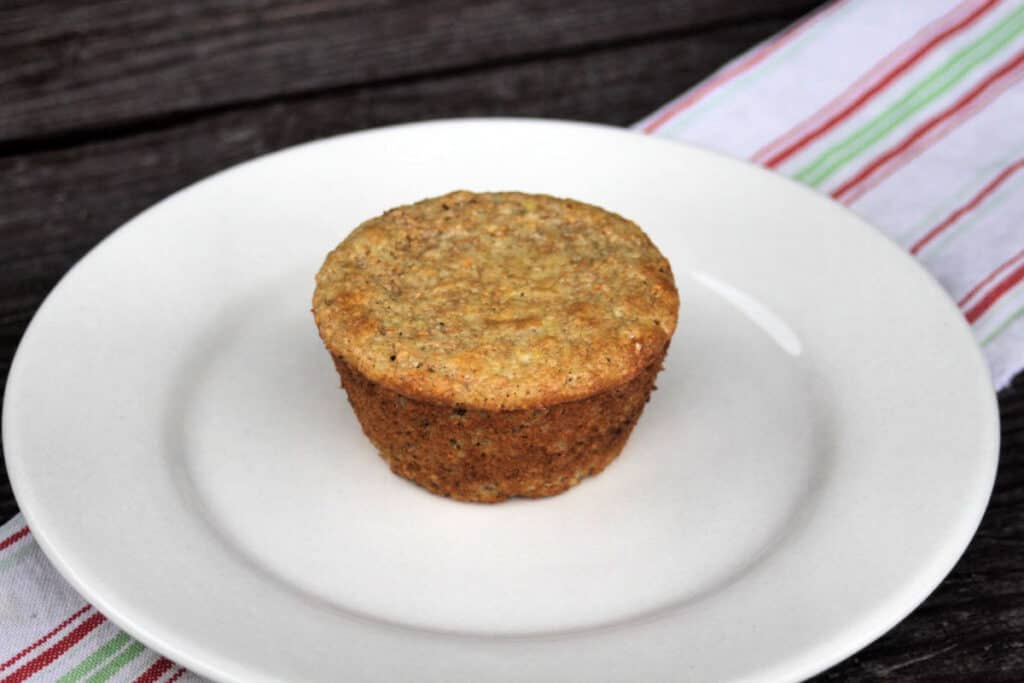 A single yogurt bran muffin sitting on a white plate on top of a red and white striped towel. 