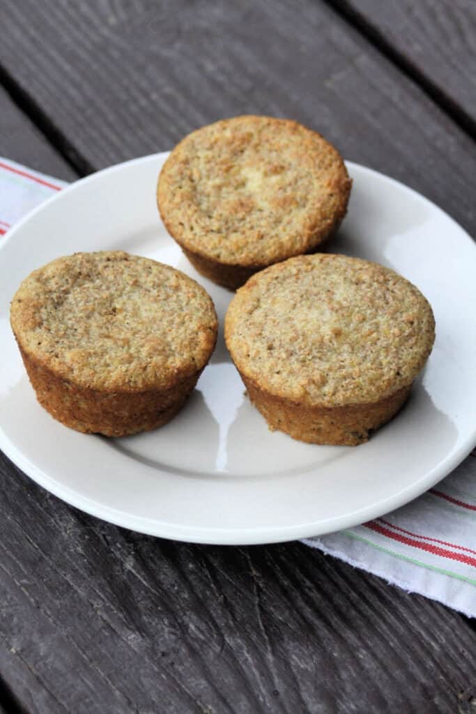 3 yogurt bran muffins sitting on a white plate on top of a red and white striped towel. 