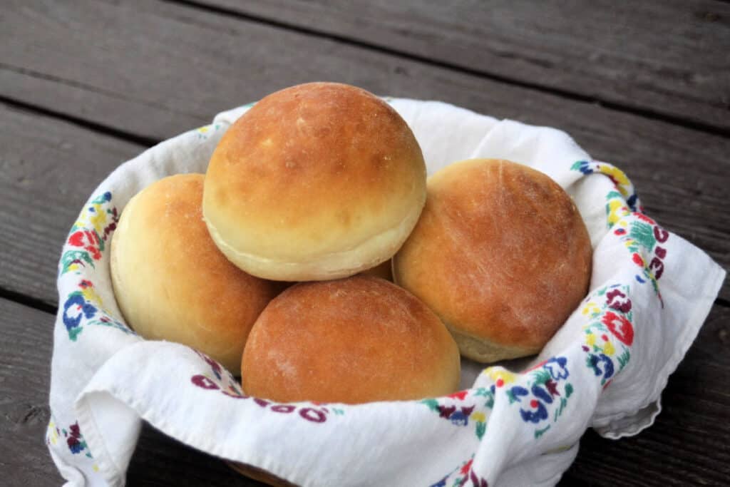 A floral linen lined basket full of yogurt dinner rolls. 