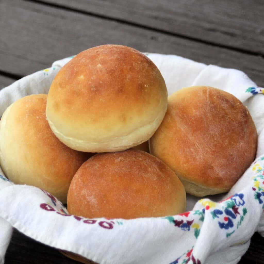 A linen lined basket full of yeast dinner rolls.