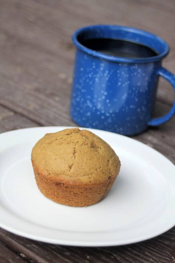 A coffee muffin on a white plate with a blue tin cup of coffee sitting behind it.
