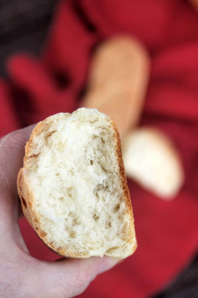 A woman's hand holding a loaf of french bread exposing the interior.