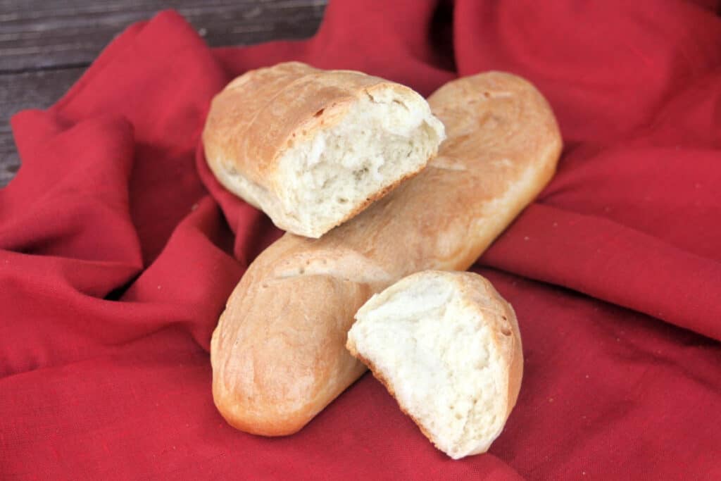 Pieces of french bread sitting on top of a whole loaf on a red cloth