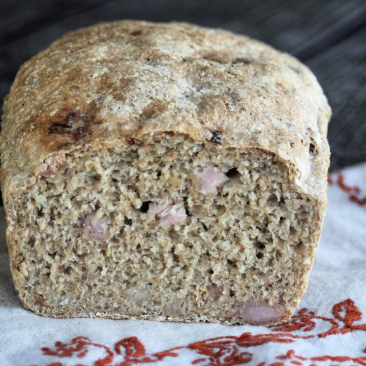 A loaf of ham bread with end cut off exposing bits of ham inside bread on an embroidered napkin.