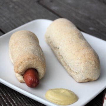 Two homemade pigs in a blanket on a white plate with mustard.