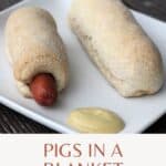 Hot dogs wrapped in bread dough on a plate with some mustard and text overlay reading: homemade pigs in a blanket.