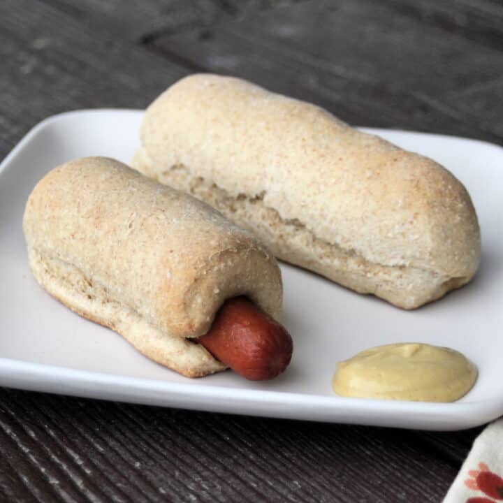 Two handmade pigs in a blanket on a white plate with mustard.