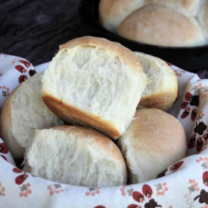 A close up of a yeast roll sitting on top of a basket of rolls lined with a napkin.
