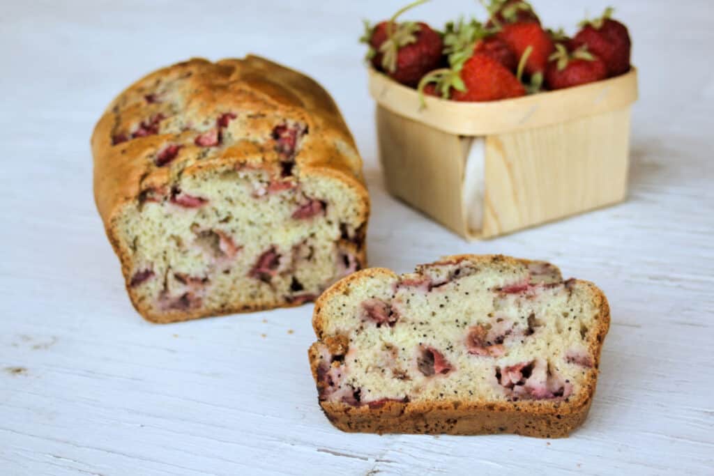 slices of strawberry bread sitting in front of the loaf and a basket of fresh strawberries.