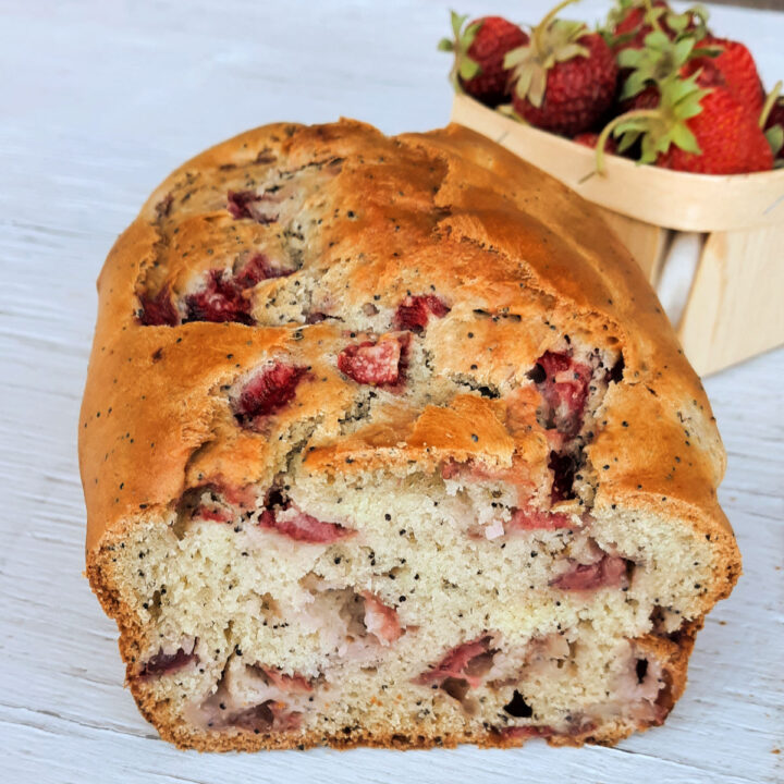 Strawberry quick bread on a white board with a basket of fresh strawberries behind it.