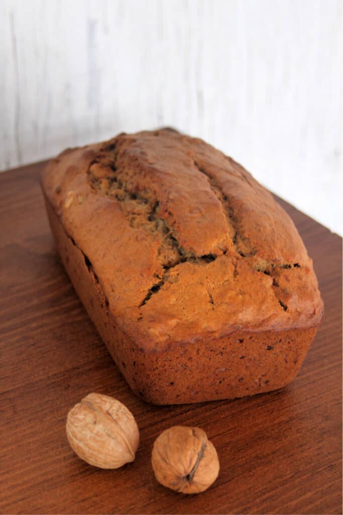 a loaf of banana bread on a table with walnuts still in shell.