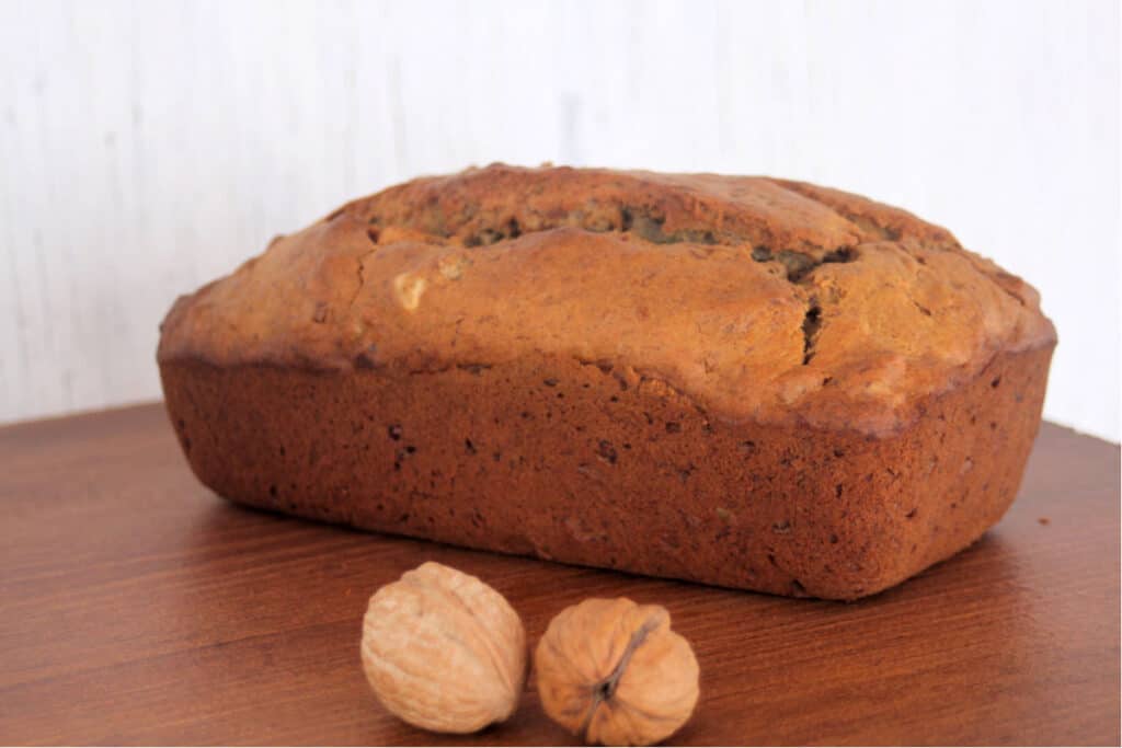 a loaf of banana bread on a table with walnuts still in shell.