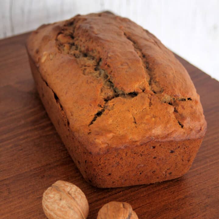 a loaf of banana bread on a table with walnuts still in shell.
