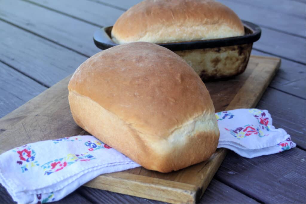 2 loaves of buttermilk bread on a cutting board with a floral napkin and text overlay.