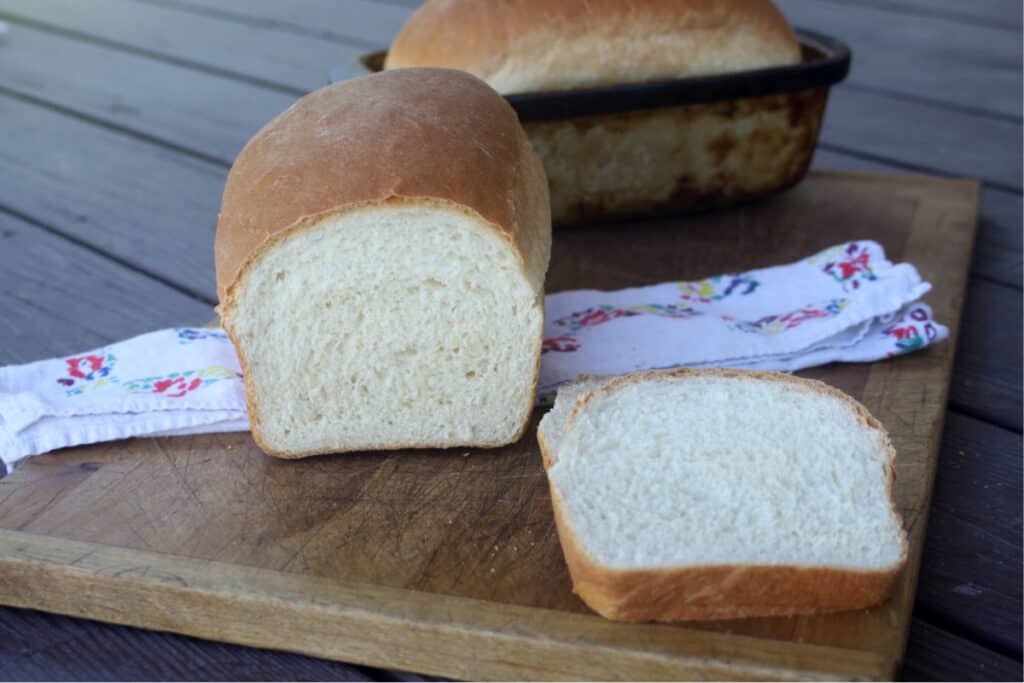 slices of buttermilk bread on a wooden cutting board sitting in front of the rest of the loaf.