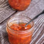Carrot jam in an open a jar with a spoon inside it, sitting in front of a sealed jar.