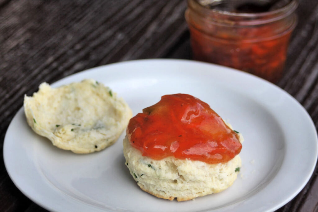 A chive biscuit spread with carrot jam on a white plate.