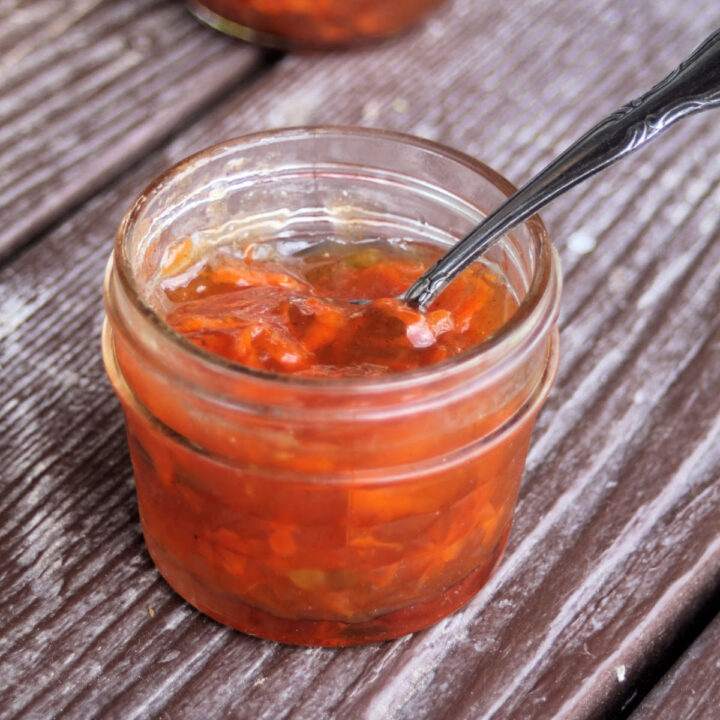 Carrot jam in an open a jar with a spoon inside it.