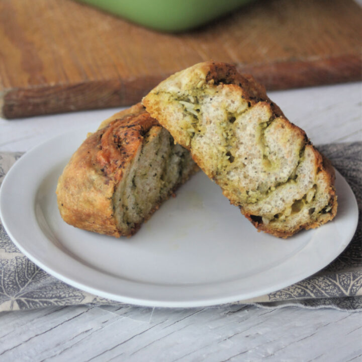 A cheesy pesto roll sliced in half on a white plate sitting on top a napkin.