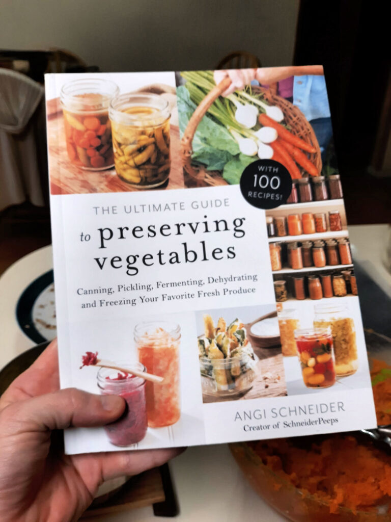 A woman's hand holding the book, The Ultimate Guide to Preserving Vegetables.