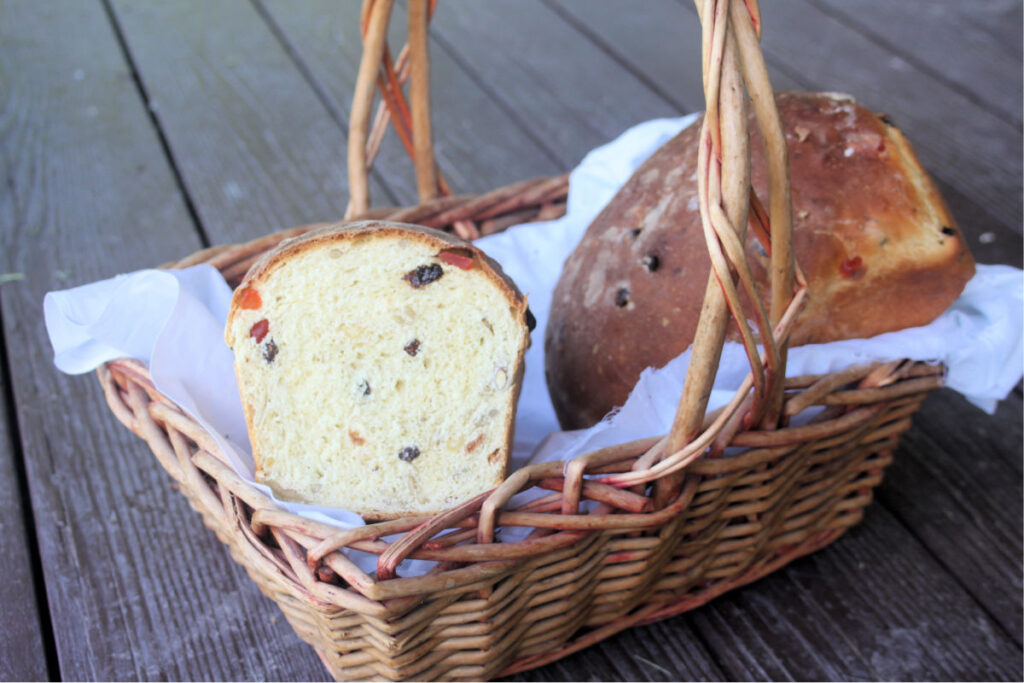 2 loaves of harvest bread in a white linen lined basket, 1 loaf has the end cut off exposing the insides.