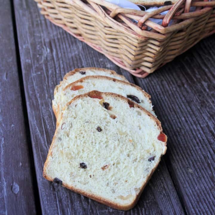 slices of harvest bread stacked on a wooden table in front of a wicker basket.