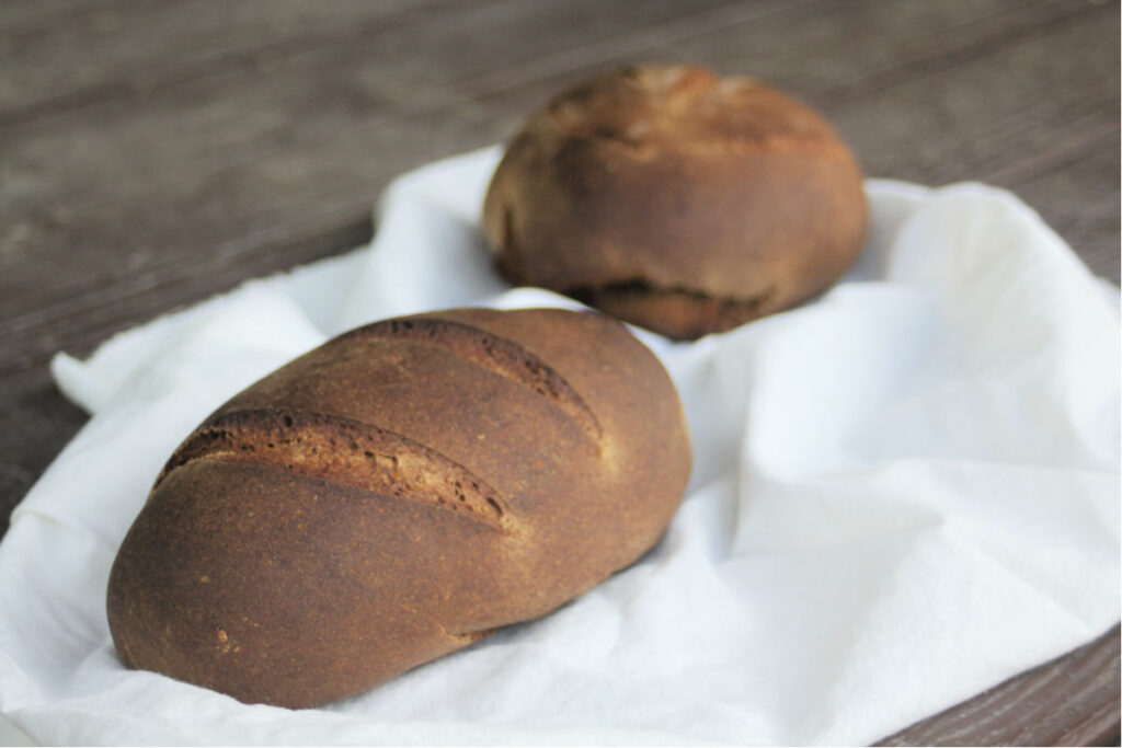 2 loaves of pumpernickel bread on a crumpled white cloth.