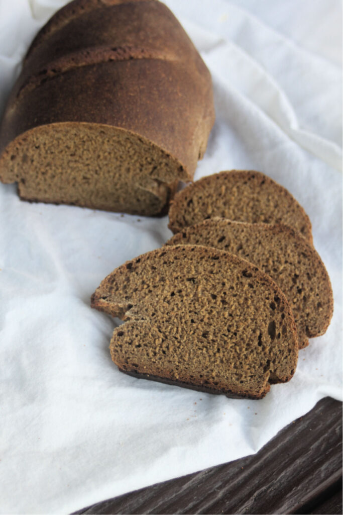 slices of pumpernickel bread on a white crumbled cloth next to the remaining loaf.