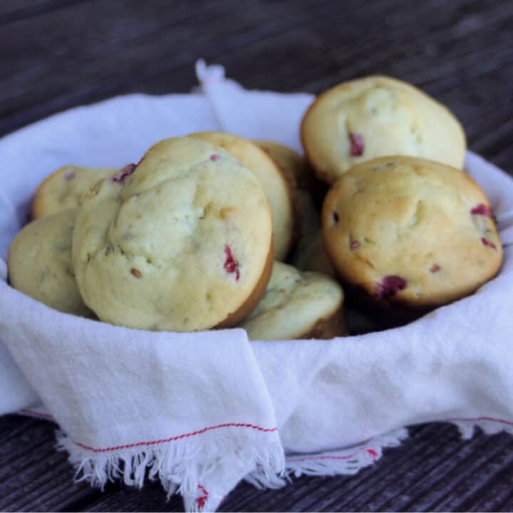 A white napkin lined basket full of raspberry cream cheese muffins.
