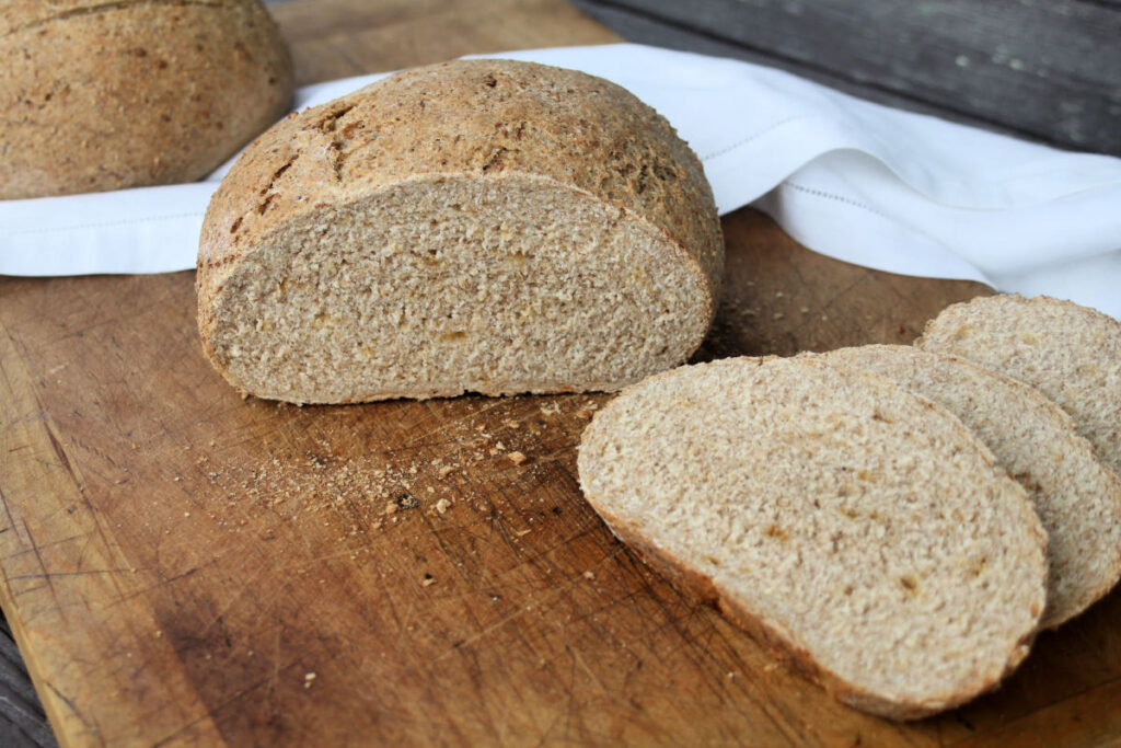 A loaf of bread on a cutting board with slices and a white napkin.