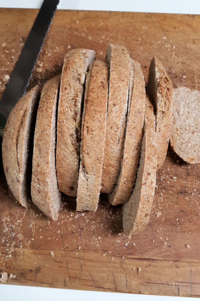 An entire loaf of whole grain cheddar bread sliced on a board. 